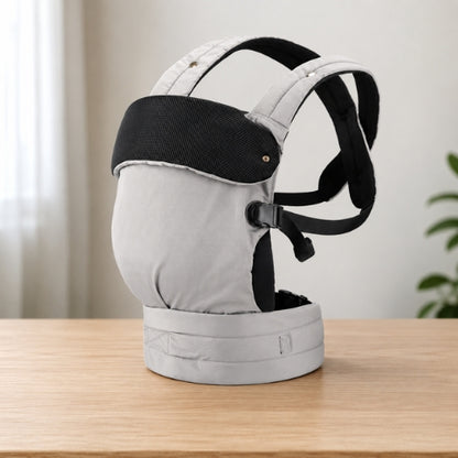 Porte bébé ventral et dorsal gris avec bretelles croisées, présenté seul sur une table