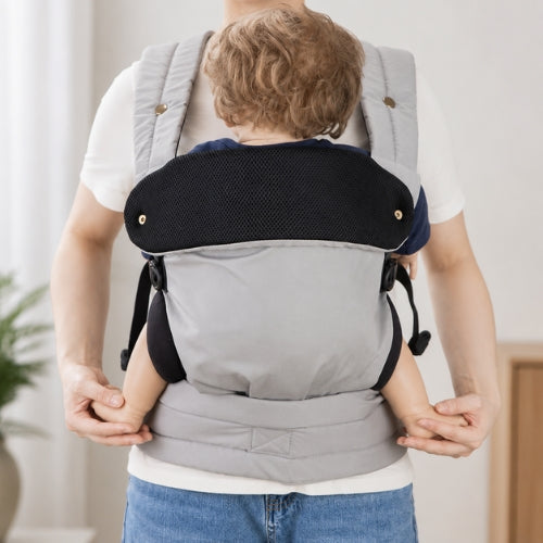 Porte bébé ventral et dorsal gris porté face à face, vue de face en intérieur