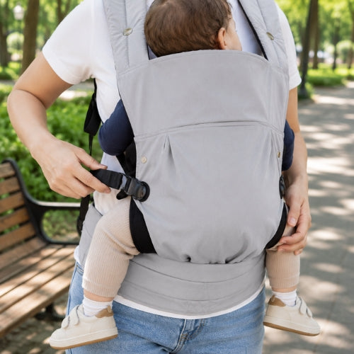 Porte bébé ventral et dorsal gris porté en extérieur, vue de face avec sangle latérale