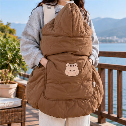 Cape porte-bébé hiver écureuil café, avec capuche relevée, tissu matelassé et poche à motif écureuil, photographiée près d’un lac.