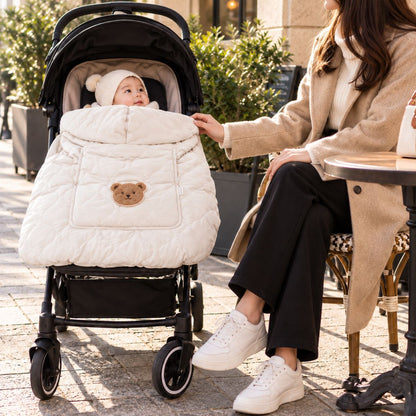 Cape porte-bébé hiver ours beige installée sur une poussette, avec tissu matelassé, motif ours et bébé au visage dégagé.