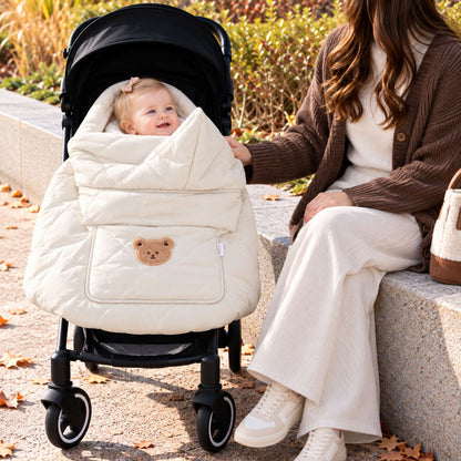 Cape porte-bébé hiver ours beige utilisée sur une poussette en promenade, avec bébé au visage visible et motif ours sur la poche avant.