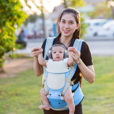 Femme portant un bébé équipé d’un casque anti bruit bébé gris, parfait pour les environnements bruyants comme les parcs ou les rues animées