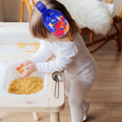 Bébé portant un casque anti-bruit enfant bleu avec motifs orange et rouge SilenceZen, jouant calmement avec des pâtes, parfait pour offrir une tranquillité sonore lors des activités à l'intérieur