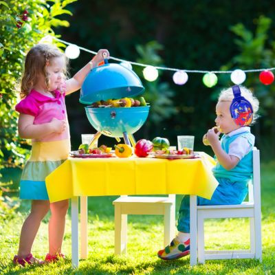 Enfants à table dans un jardin, avec un enfant portant un casque anti-bruit enfant bleu aux motifs orange et rouge SilenceZen, conçu pour réduire les bruits forts et offrir une tranquillité sonore en extérieur