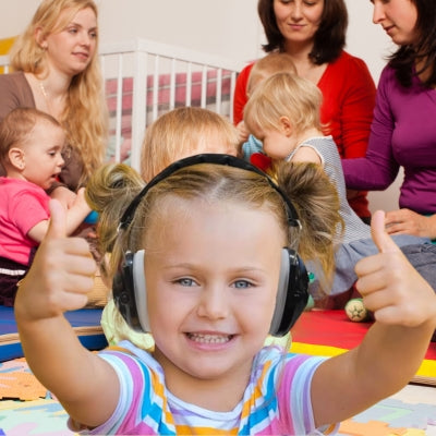 Une petite fille portant un casque antibruit enfant noir SilenceAnge dans une crèche animée, profitant d’un environnement paisible pour jouer et apprendre