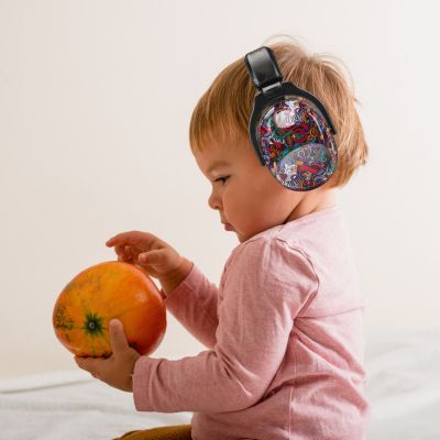 Bébé portant un casque anti-bruit enfant noir avec motifs musicaux multicolores SilenceZen, explorant un fruit en toute tranquillité, conçu pour protéger ses oreilles sensibles tout en favorisant son développement