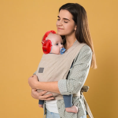 Un enfant dans un champ, porté par sa mère et équipé d’un casque antibruit enfant noir SilenceAnge, pour des moments calmes et sereins en extérieur