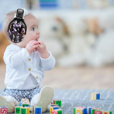 Bébé portant un casque anti-bruit enfant noir avec motifs violet et orange SilenceZen, jouant avec des blocs à la maison, idéal pour offrir un calme absolu et un confort optimal