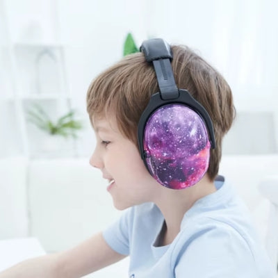 Garçon concentré portant un casque anti bruit enfant violet au motif galaxie, conçu pour améliorer la concentration dans des environnements calmes