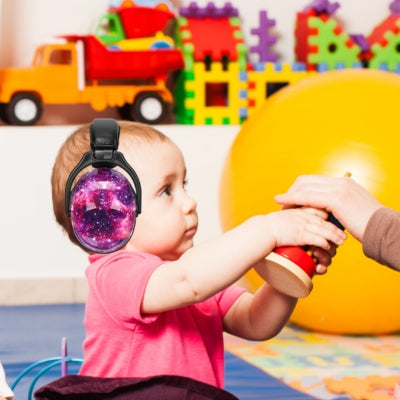 Bébé dans une salle de jeux colorée, portant un casque anti bruit enfant violet au motif galaxie, conçu pour protéger son audition tout en explorant des activités ludiques