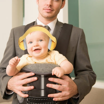 Bébé portant un casque antibruit pour bébé jaune JauneCocon, assis confortablement dans un porte-bébé pour des sorties agréables