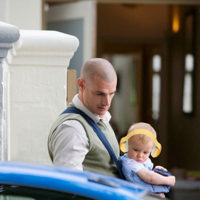 Papa portant un bébé équipé d'un casque antibruit pour bébé jaune JauneCocon pour une protection sonore optimale dans un environnement urbain