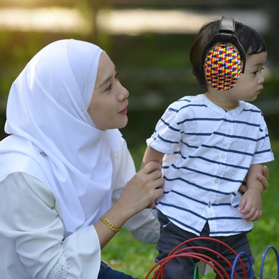 Mère et enfant jouant en plein air, l’enfant portant un casque antibruit enfant avec un design puzzle multicolore, idéal pour protéger les oreilles lors d’activités extérieures