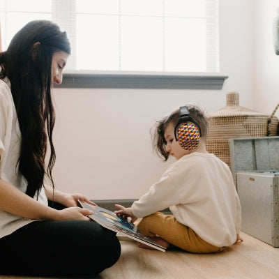 Mère et enfant partageant un moment de lecture calme, l’enfant portant un casque antibruit enfant avec un motif puzzle multicolore, conçu pour un environnement serein