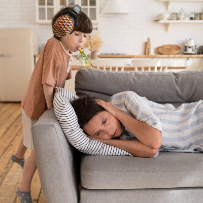 Un enfant soufflant dans une langue de fête, équipé d’un casque antibruit enfant au motif puzzle multicolore, idéal pour réduire efficacement les bruits lors de moments bruyants