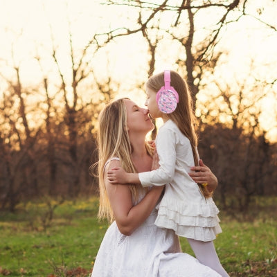 Mère et fille partageant un moment au coucher du soleil, la fille portant un casque antibruit enfant rose avec un design licorne, parfait pour les enfants en quête de confort et de magie