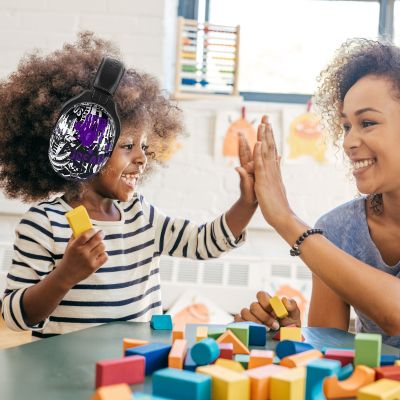 Enfant portant un casque antibruit enfant VioletEdge violet, jouant avec des blocs colorés dans une ambiance joyeuse, tout en bénéficiant d’un confort optimal grâce aux coussinets ergonomiques