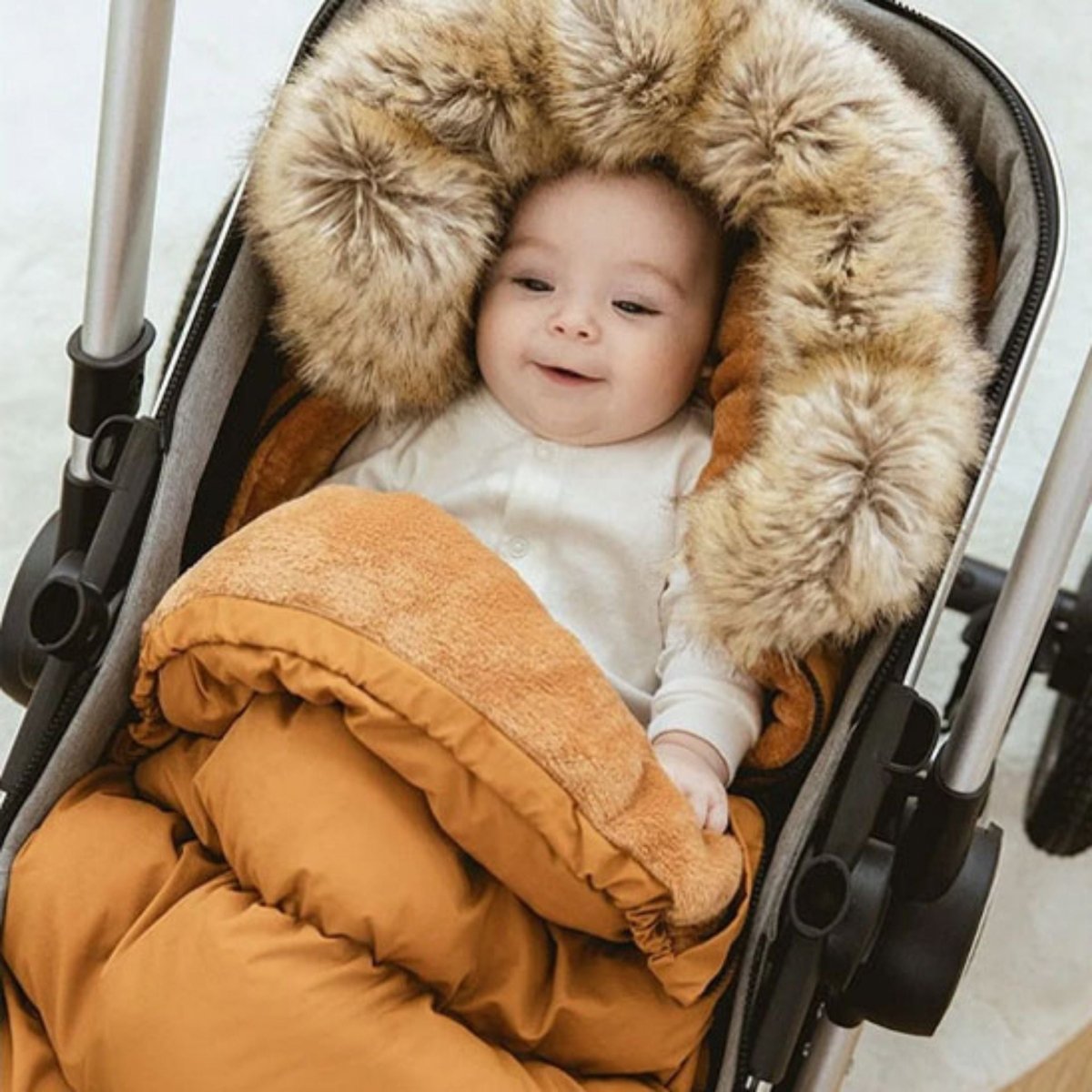 bébé souriant installé dans une chanceliere bebe marron cocon avec intérieur doux et capuche large