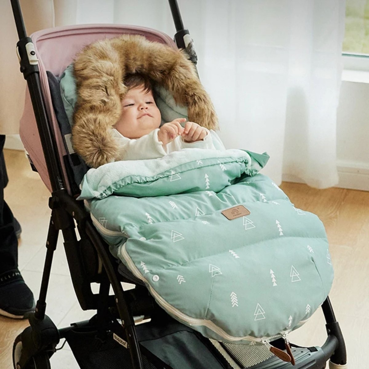 chanceliere bebe avec motif triangle vert, noir et marron, bébé allongé en poussette avec capuche en fausse fourrure