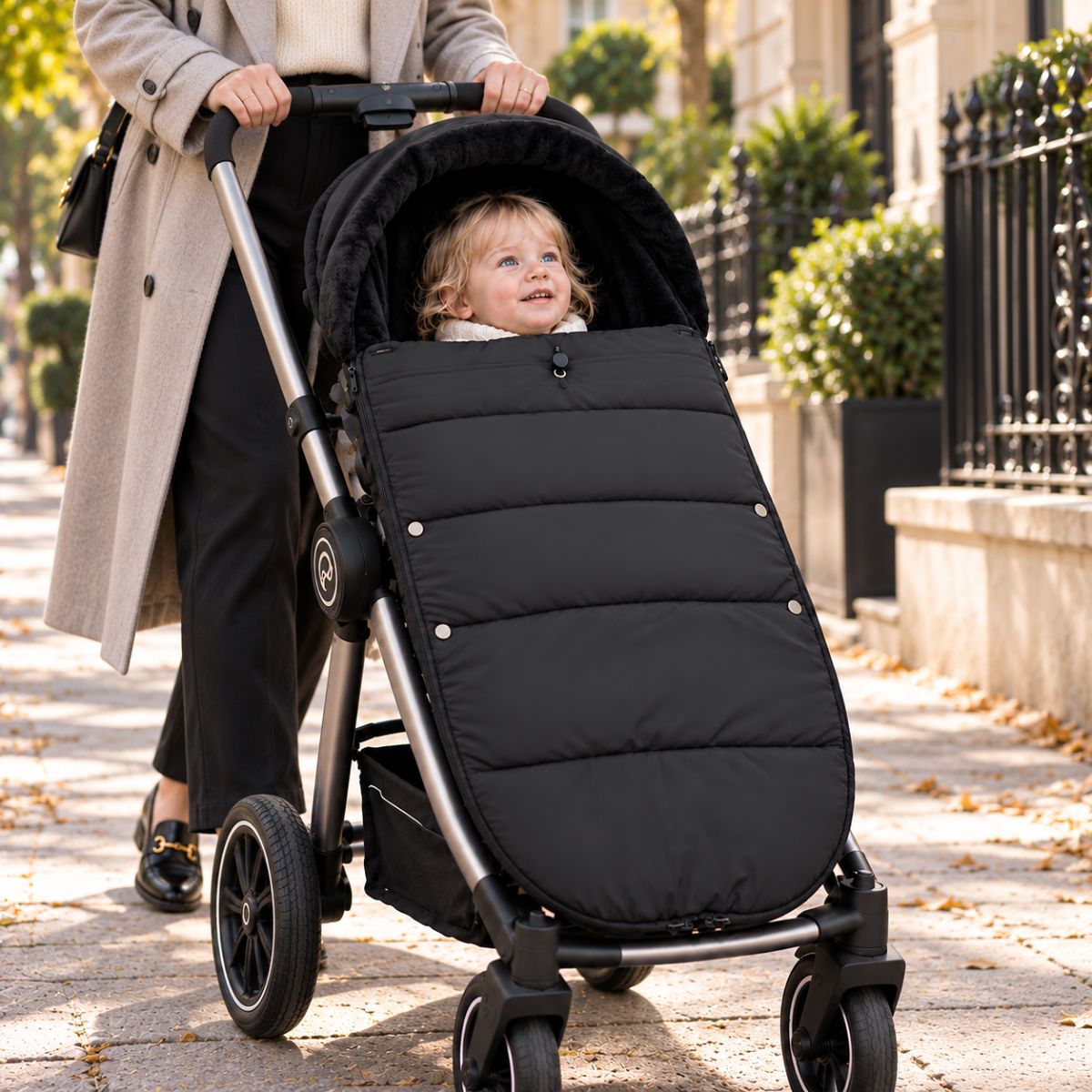 Chancelière noire avec intérieur doux, bébé installé avec sa maman pendant une sortie urbaine
