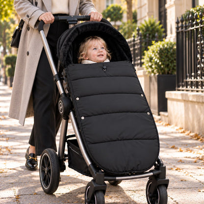 Chancelière noire avec intérieur doux, bébé installé avec sa maman pendant une sortie urbaine