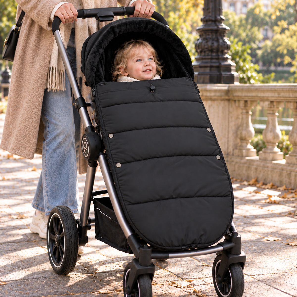Chancelière noire avec intérieur doux, bébé installé avec sa maman lors d’une promenade en ville
