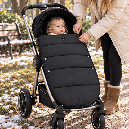 Chancelière noire avec intérieur doux, bébé installé dans une poussette pendant une sortie avec de la neige au sol