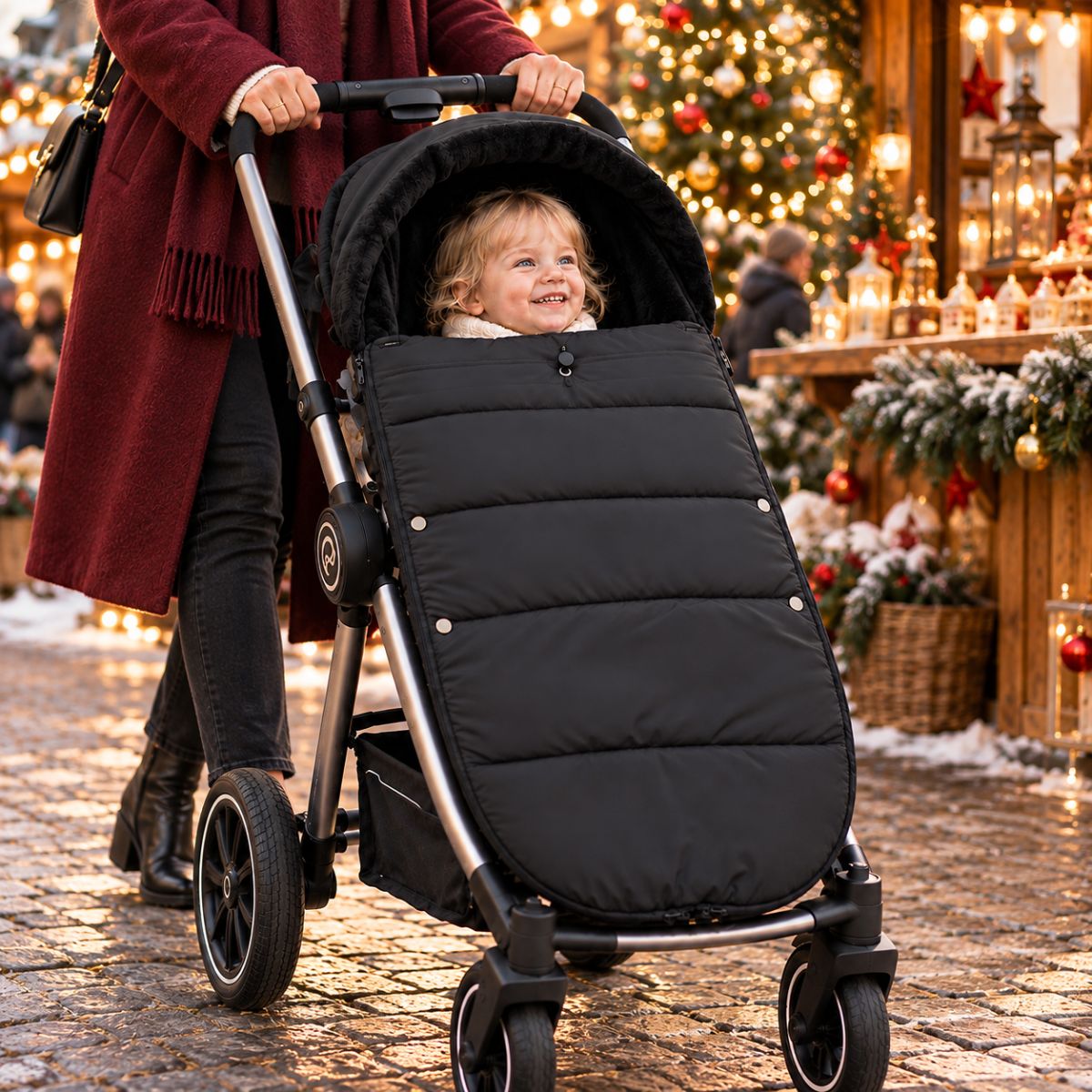 Chancelière noire avec intérieur doux, bébé installé avec sa maman devant un marché de Noël