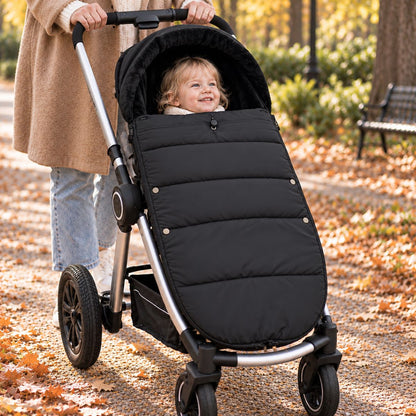Chancelière noire avec intérieur doux, bébé installé dans une poussette lors d’une sortie au parc en automne