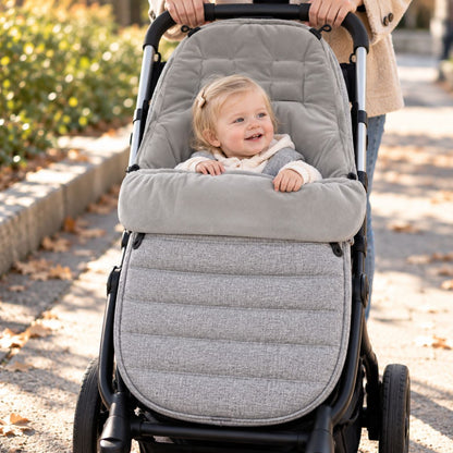 Chancelière évolutive gris clair installée sur une poussette avec bébé pendant une promenade