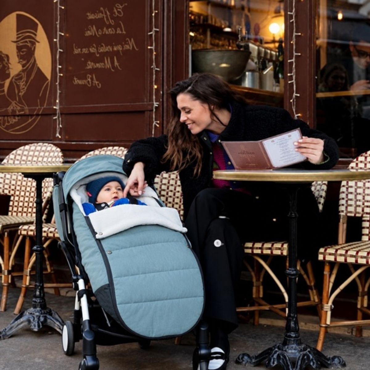 Chanceliere impermeable poussette Aqua avec bébé installé devant un café