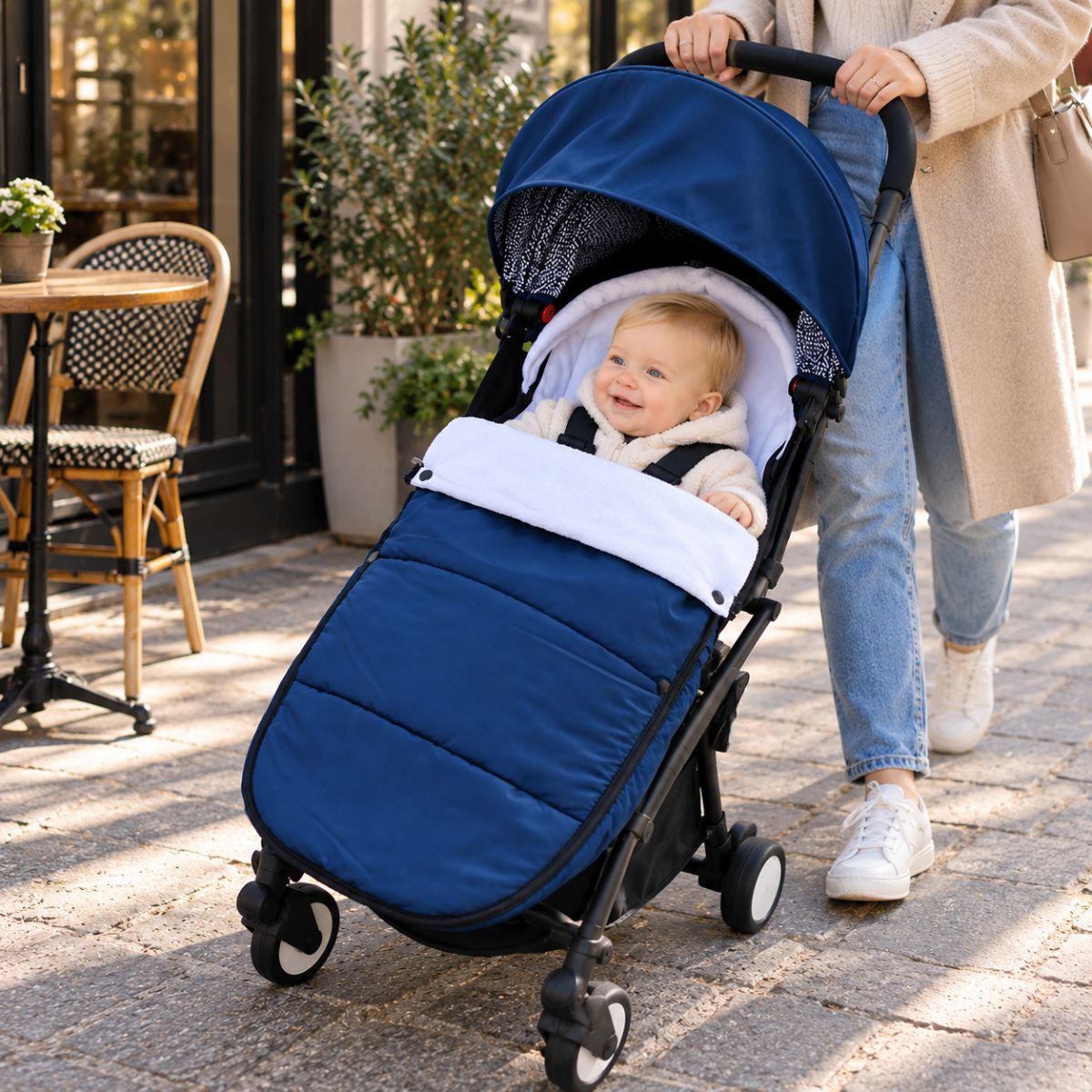 Chanceliere impermeable poussette bleu marine avec bébé installé lors d’une promenade près d’un café