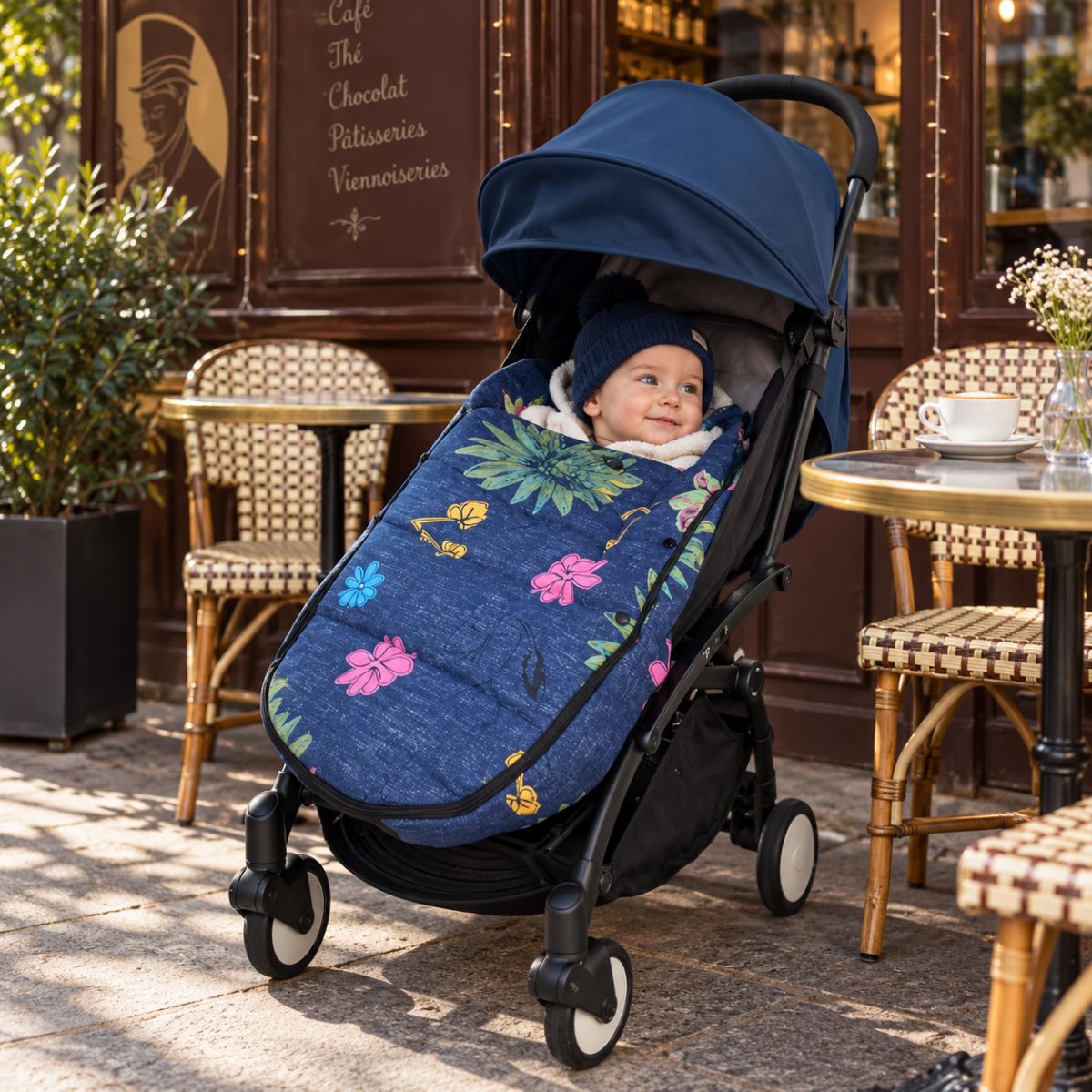Chanceliere impermeable poussette bleu marine fleurie avec bébé installé devant un café