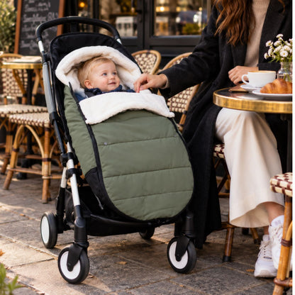 Chanceliere impermeable poussette olive avec bébé installé devant un café