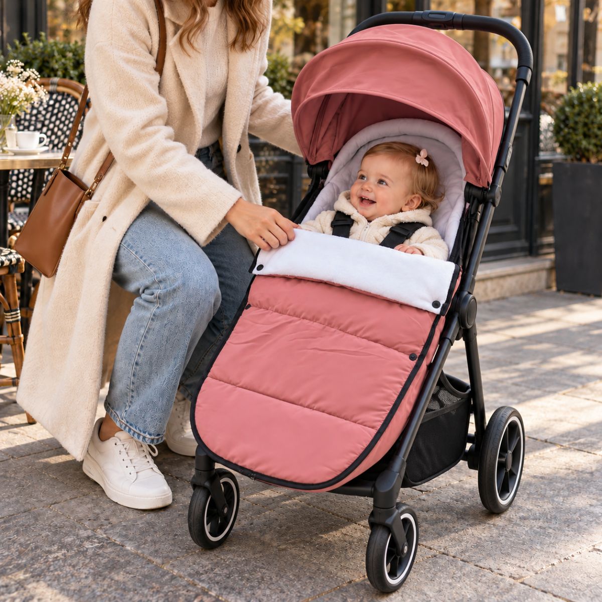 Chanceliere impermeable poussette rose avec bébé installé près d’un café