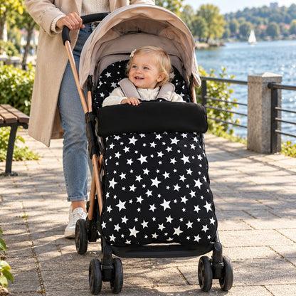 Chancelière polaire noire à étoiles installée sur une poussette avec bébé au bord du lac