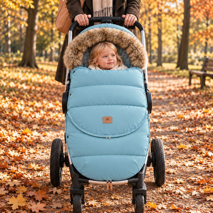 Chancelière poussette bleu clair avec col effet fourrure, bébé installé dans une poussette vue de face dans un parc en automne