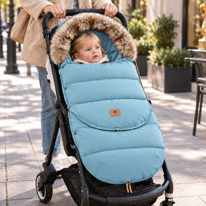 Chancelière poussette bleu clair avec col effet fourrure, bébé installé avec sa maman lors d’une sortie en ville