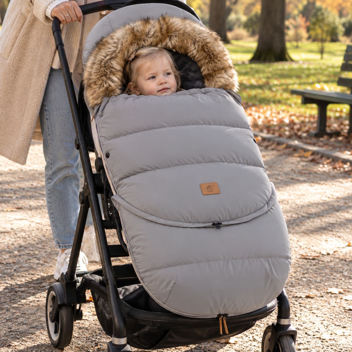 Chancelière poussette gris clair avec col effet fourrure, bébé installé avec sa maman dans un parc en automne