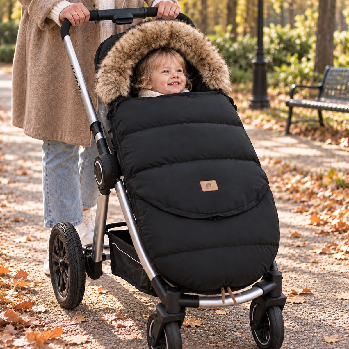 Chancelière poussette noire avec col effet fourrure, bébé installé avec sa maman lors d’une sortie en automne