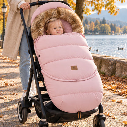 Chancelière poussette rose poudré avec col effet fourrure, bébé installé dans une poussette au bord d’un lac en automne
