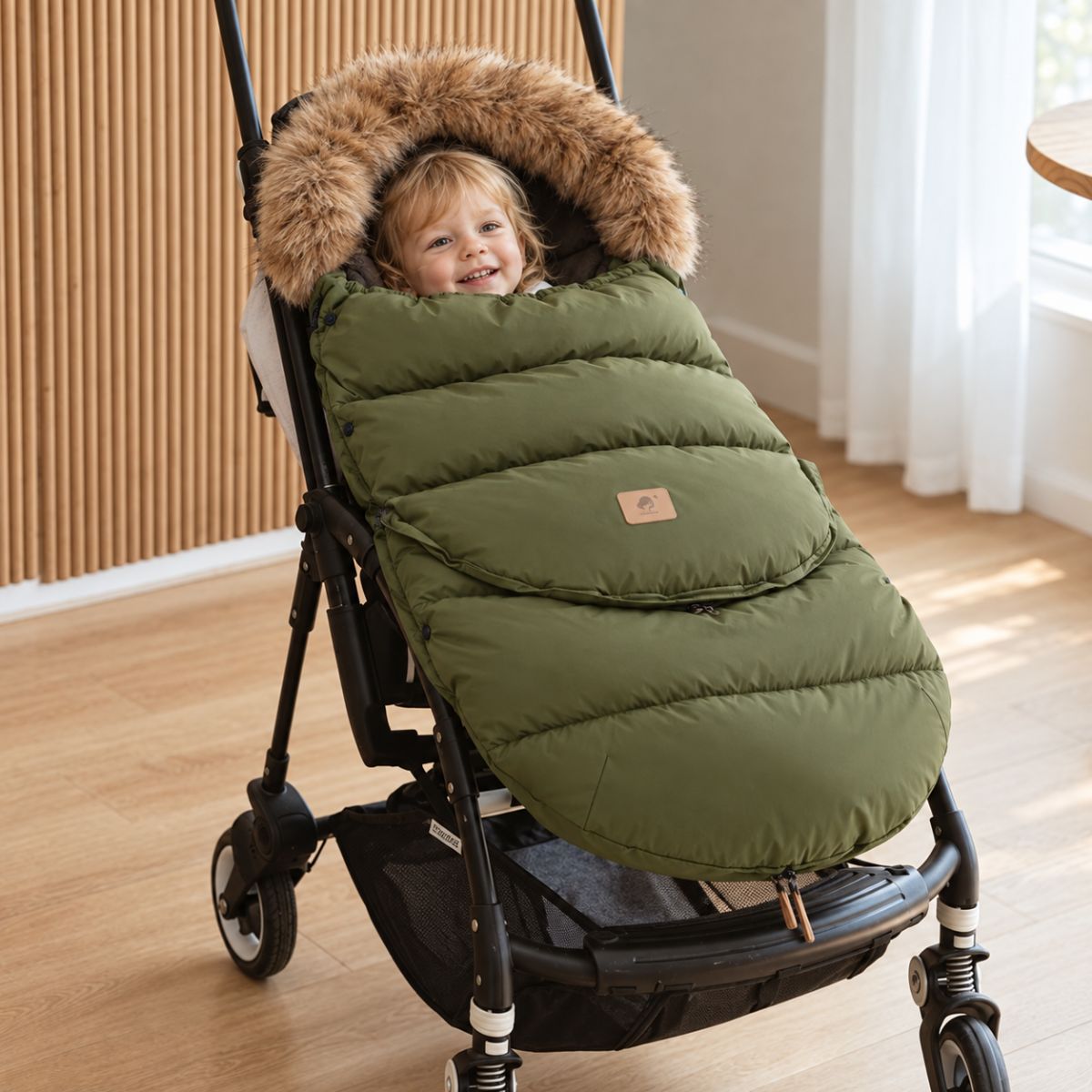 Chancelière poussette vert armée avec col effet fourrure, bébé installé dans une poussette à l’intérieur