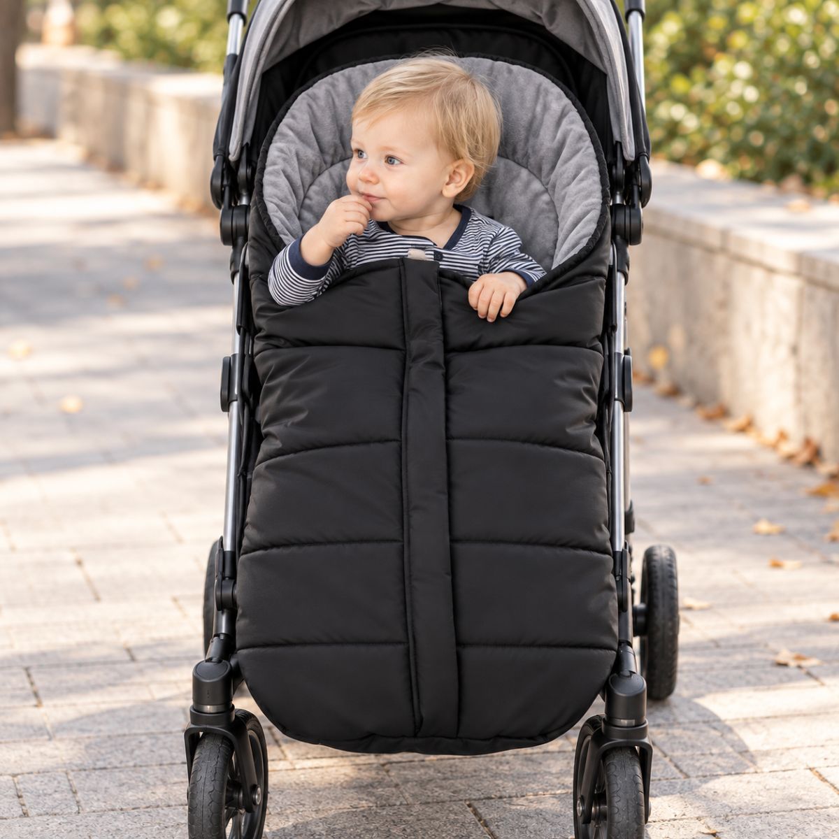 Chancelière poussette noire avec doublure polaire grise, bébé avec bonnet pendant une promenade dans la neige
