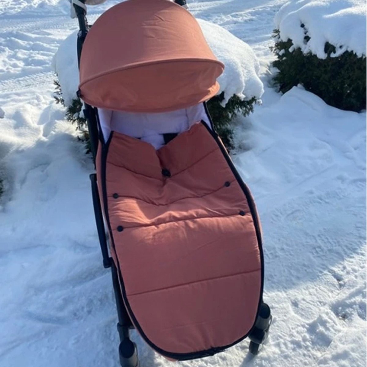 Chancelière poussette rose en tissu imperméable installée sur poussette noire dans la neige