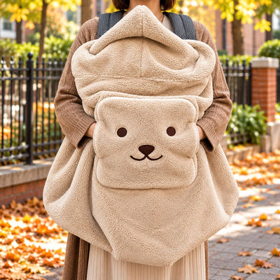 Couverture de portage moumoute beige portée devant une femme, avec texture pelucheuse, grande capuche et poche frontale à visage d’ourson