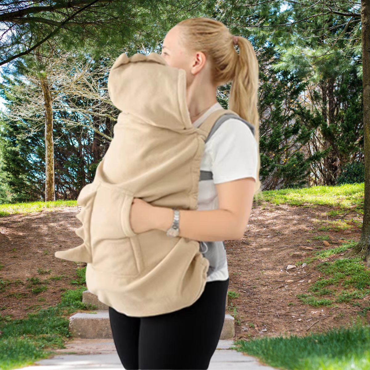 Couverture de portage polaire beige vue de profil sur un porte-bébé ventral, avec capuche à crête dinosaure et poche pour les mains