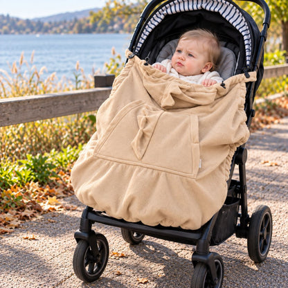 Couverture de portage polaire beige installée sur une poussette près d'un lac, avec poche frontale et bébé au visage visible