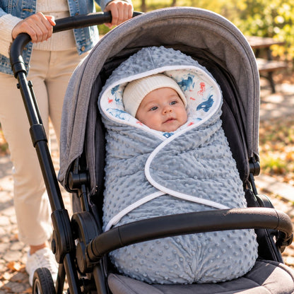 Couverture nomade bébé bleu-gris avec capuche à motifs marins, pans rabattables et bordure blanche, dans une poussette grise