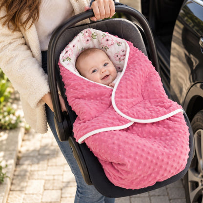 Couverture nomade bébé rose floral à capuche, avec pois en relief et bordure blanche, présentée dans une coque bébé